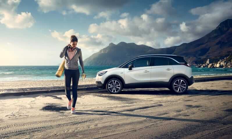 A woman is going on the beach, her Opel Grandland X is parked